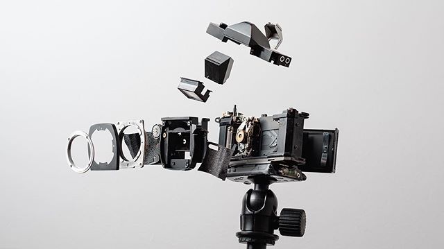An exploded view of a classic camera on a tripod against a plain white backdrop.