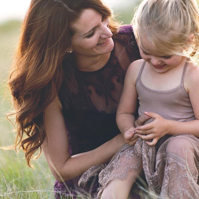 A mother and daughter share a tender moment together in a grassy field, bathed in soft, natural light.