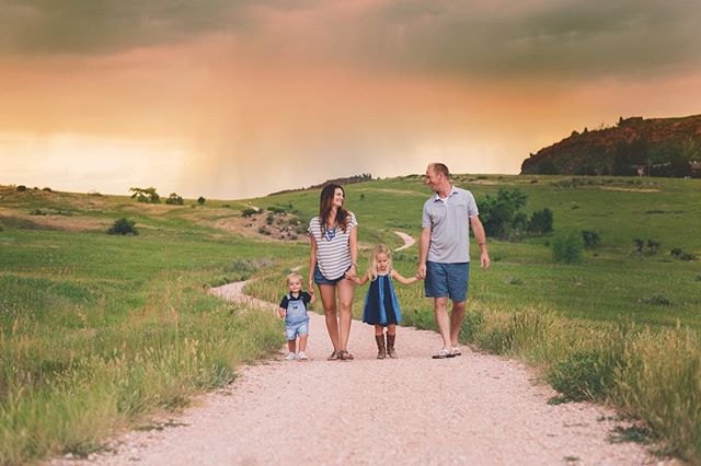 A family of four is walking on a path in a field, enjoying a sunny day together.