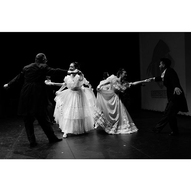 A group of dancers in vintage attire gracefully perform on a stage in a captivating black and white image.