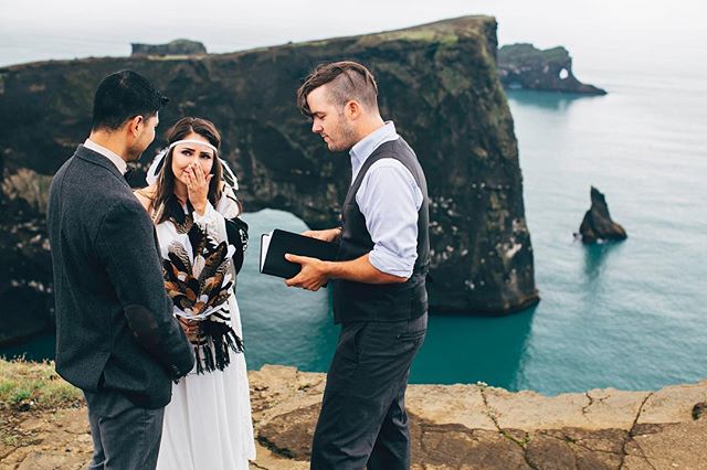 Emotional wedding ceremony on a scenic cliff overlooking the ocean with bride, groom and officiant.