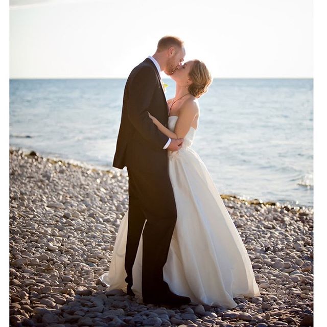 A bride and groom share a kiss on a rocky beach after their wedding ceremony in a romantic pose.