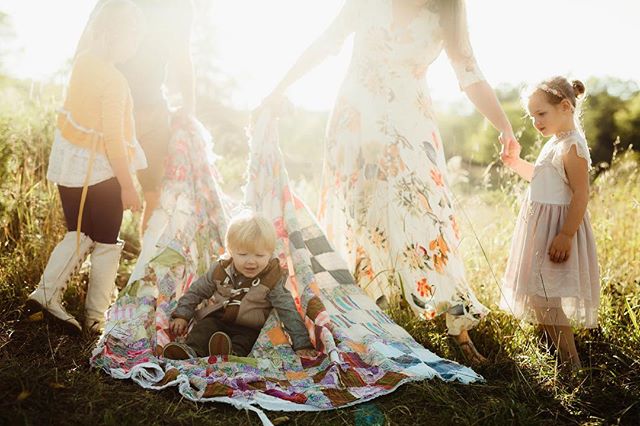 A loving family creates a cozy tent with a quilt on a sunny day in a grassy field.