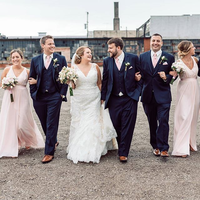 A wedding party walks together smiling, with the bride and groom in the center.