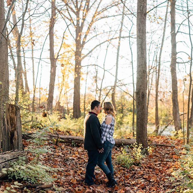A couple stands face-to-face in an autumn forest, bathed in soft, warm light.