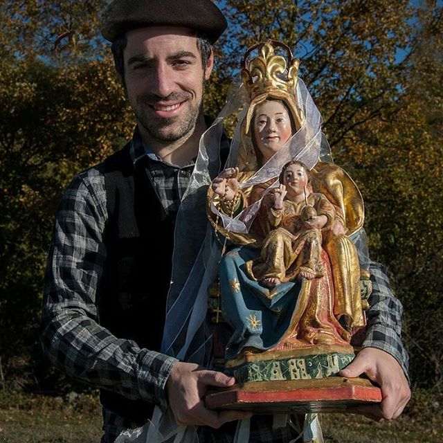 A man smiles while holding a Virgin Mary statue in a park.