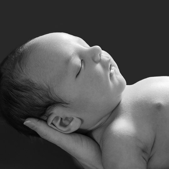 A serene black and white portrait of a newborn baby sleeping peacefully in someone's hand.