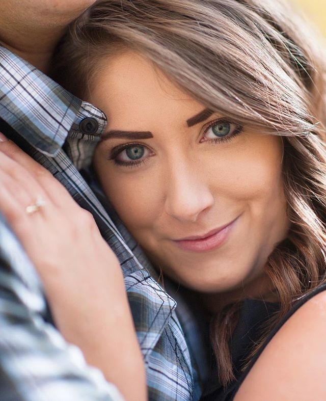 A woman with an engagement ring leans affectionately against her partner in a plaid shirt.