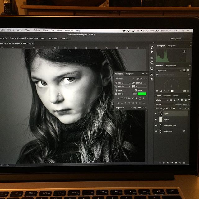 A black and white portrait of a young girl being edited in Adobe Photoshop on a laptop.