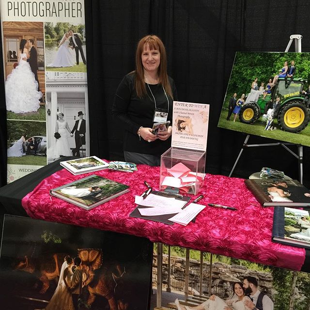 A wedding photographer stands at her booth displaying her work and promotional material.