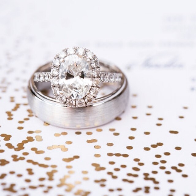 A pair of wedding rings, including a stunning diamond engagement ring, sparkles against a confetti-scattered background.