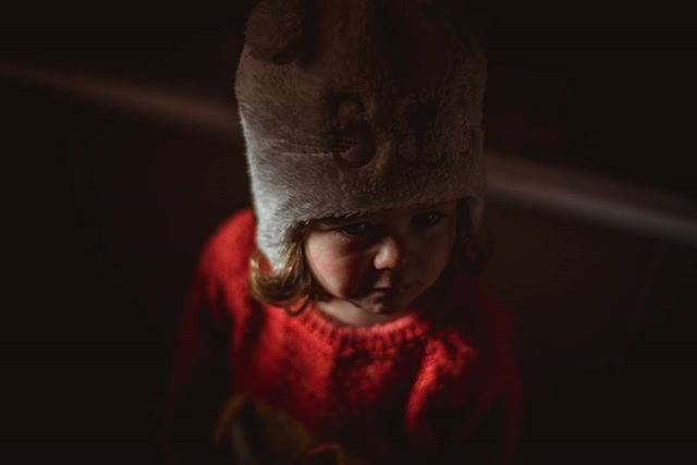 A young child with a furry hat and red sweater looks down, creating an intimate and emotional portrait.