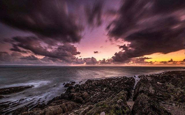 Dramatic sky over a rocky coastline and tranquil sea, showcasing a serene and moody landscape at dusk.