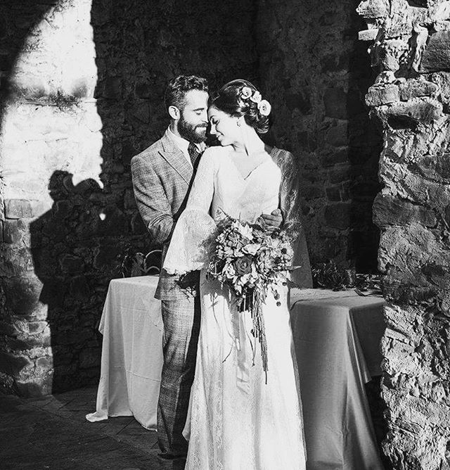 A bride and groom embrace during their wedding, holding a bouquet in an intimate indoor setting.