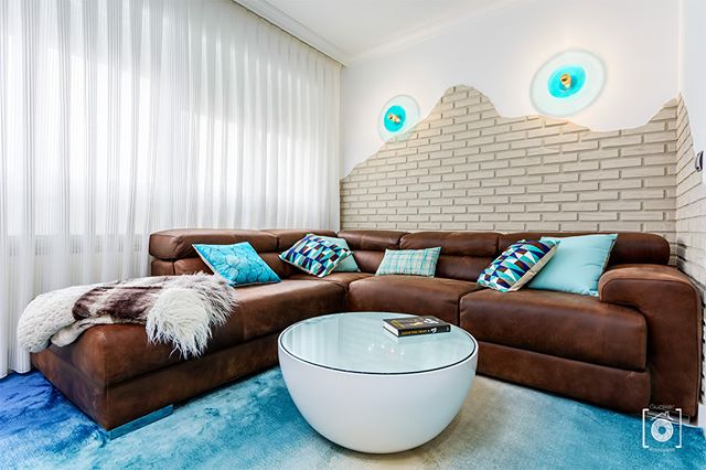 A modern living room features a brown leather couch, round coffee table, and stylish wall lights.