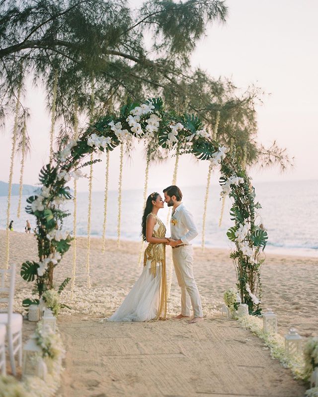 A bride and groom share a tender moment under a floral arch at their beach wedding.
