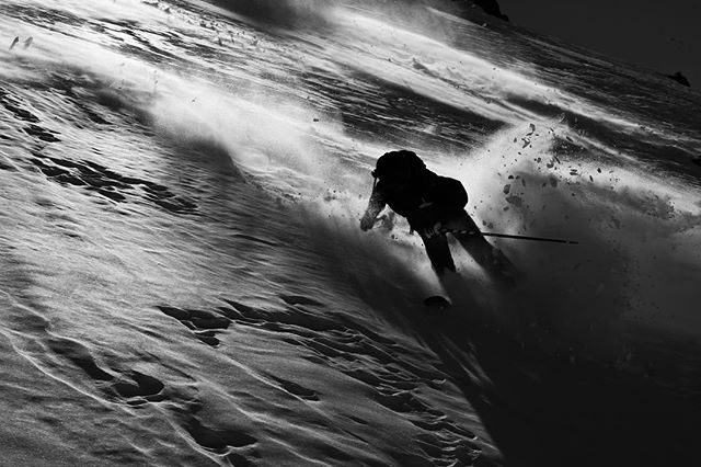 A skier is captured speeding down a snowy mountain in a black and white, high-angle shot showcasing motion and power.