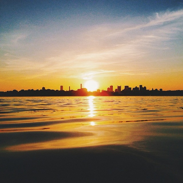 A scenic sunset view over the water, with a silhouetted city skyline on the horizon creating a tranquil urban landscape.