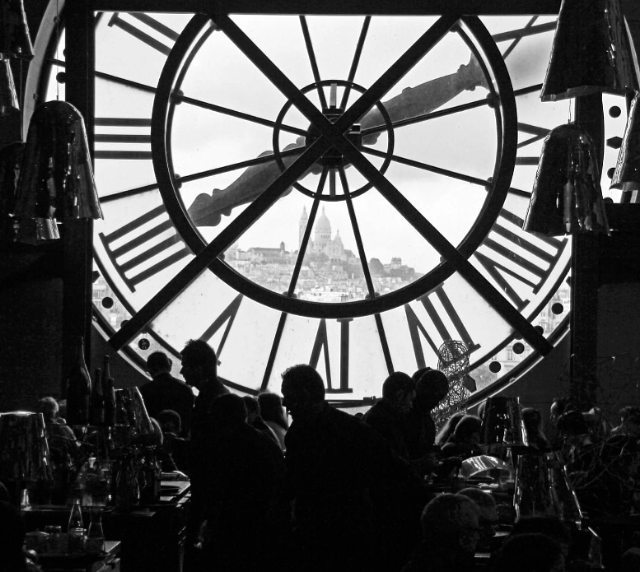 A large clock frames a Parisian cityscape with people dining below, capturing a vintage and dreamy scene.