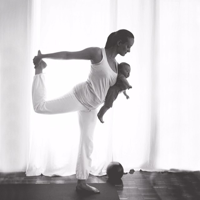 A woman practices yoga while holding her baby, promoting wellness and motherhood.