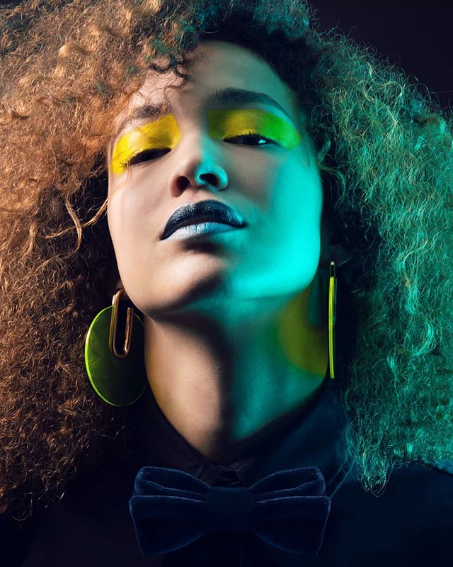 A woman with dramatic makeup poses in a vibrant, editorial style shot with a confident and intense mood.