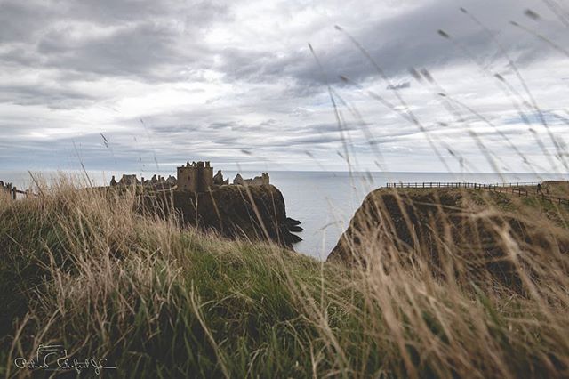 Dunnottar Castle ruins sit dramatically on a cliff overlooking the ocean in Scotland on an overcast day.