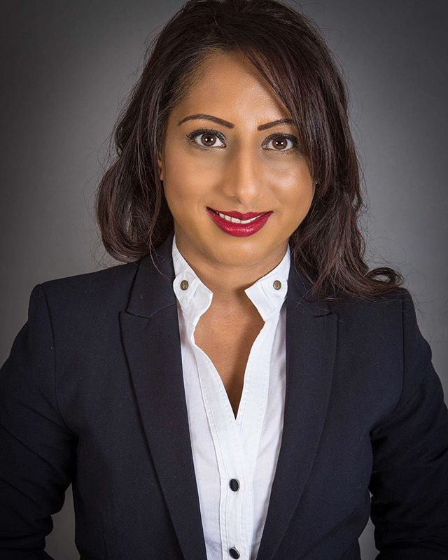 Professional portrait of a confident woman in a blazer and white shirt against a gray background.