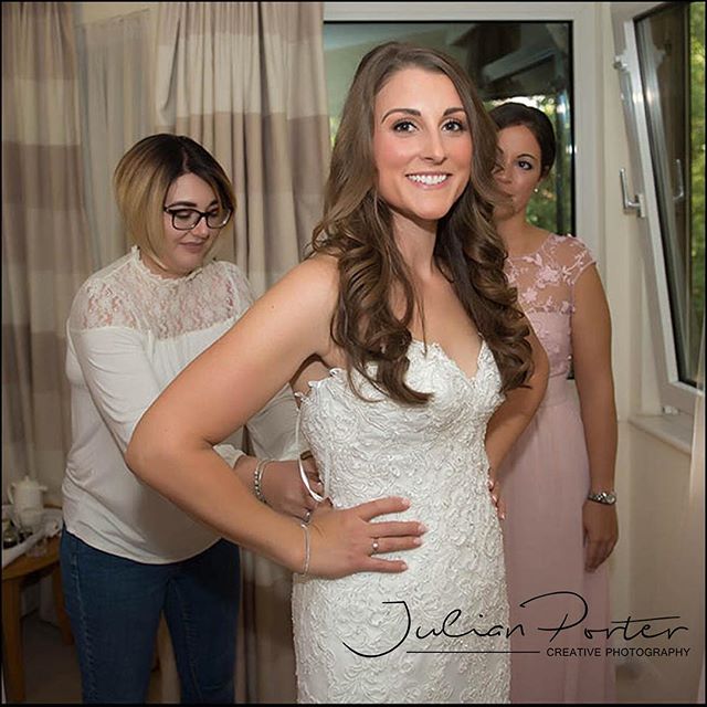 A bride smiles as she is helped into her wedding dress by her bridesmaids.