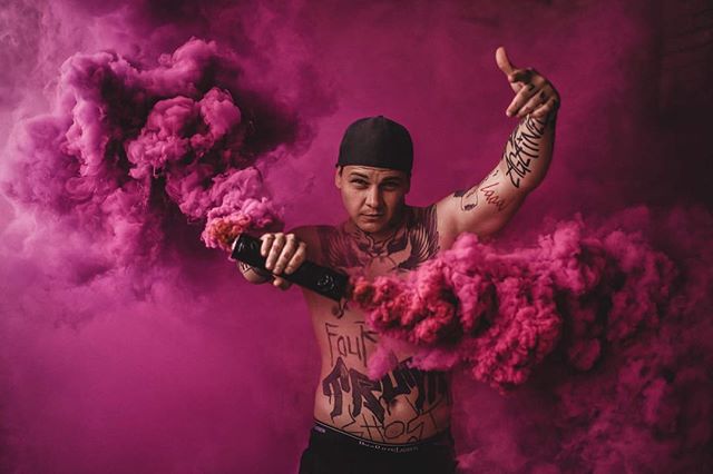 A tattooed man creates a striking image surrounded by vibrant pink and purple smoke in a studio setting.