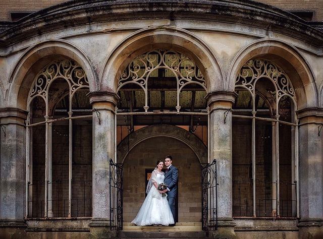 A bride and groom pose in front of an ornate architectural building on their wedding day.