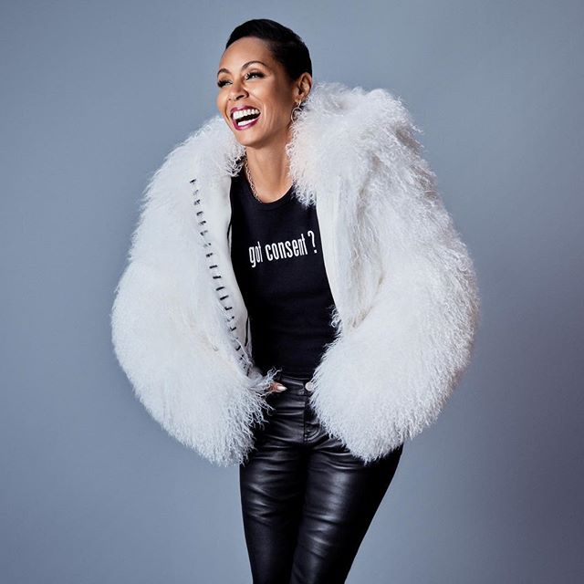 A laughing woman in a fur coat and leather pants poses in a studio.