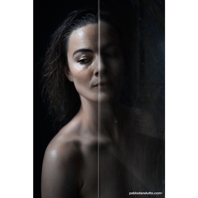 A woman's emotional studio portrait is divided by a glass surface, creating a mysterious and intimate atmosphere.