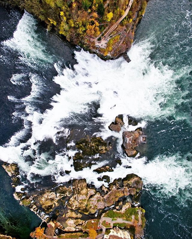 Aerial view of a powerful waterfall cascading through a rocky landscape with trees and buildings. 