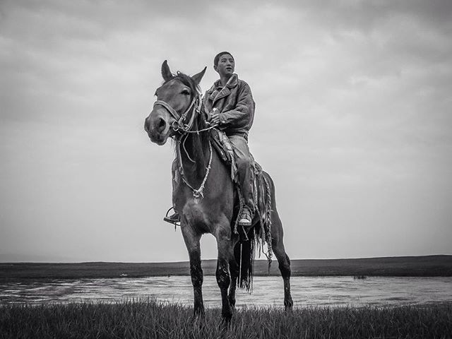 A man rides a horse across a vast field in this captivating black and white portrait.