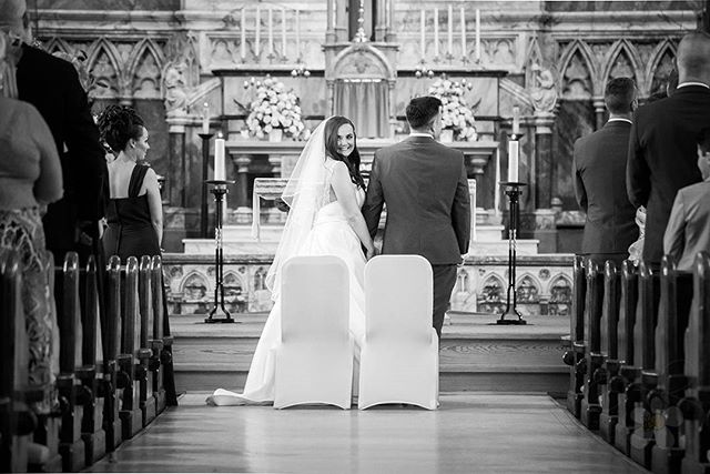 A bride and groom stand in a church aisle during their wedding ceremony.