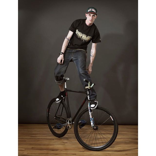 A confident man balances on a bicycle in a studio, showcasing urban style and fitness.
