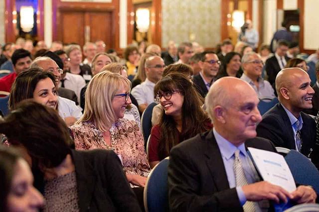 A diverse group of people attentively listen at a conference, creating a vibrant and engaged atmosphere.