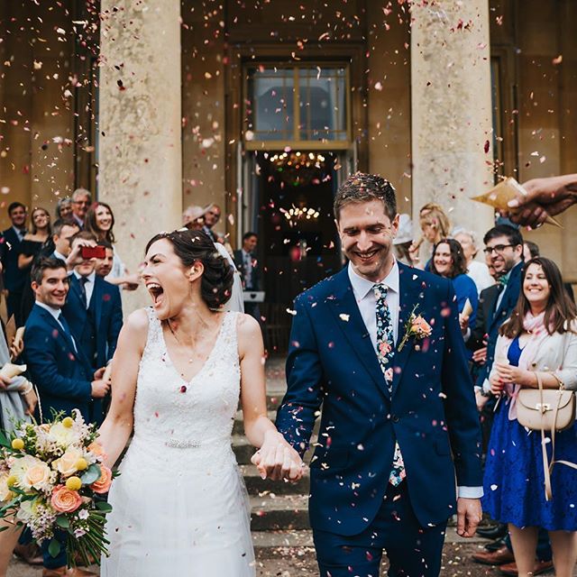 A happy bride and groom walk hand-in-hand through a shower of confetti after their wedding ceremony.