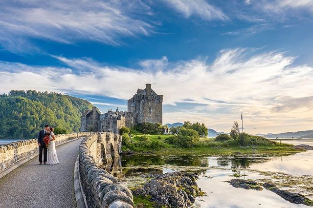A bride and groom embrace on a stone bridge with the Eilean Donan Castle in Scotland.