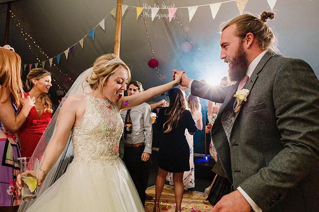 A bride and groom celebrate at their wedding reception, dancing with guests in a festive tent setting.