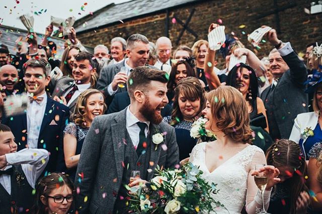 A happy bride and groom are showered with confetti at their wedding surrounded by wedding guests.