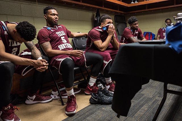 A group of basketball players sit in the locker room, showing the emotional aftermath of a game.
