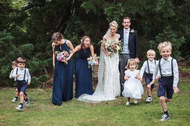 A joyful wedding party poses outdoors, with running ring bearers and smiling bridesmaids.