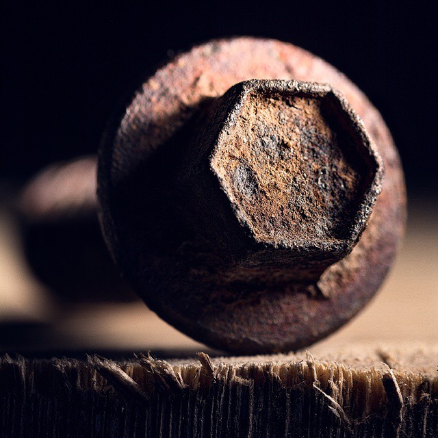 A rusty bolt with a hexagonal head sits on a wooden surface in dramatic lighting.