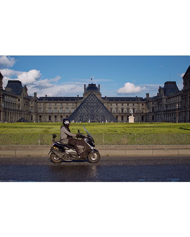 A man rides a motor scooter in front of the Louvre Museum and its iconic pyramid in Paris.