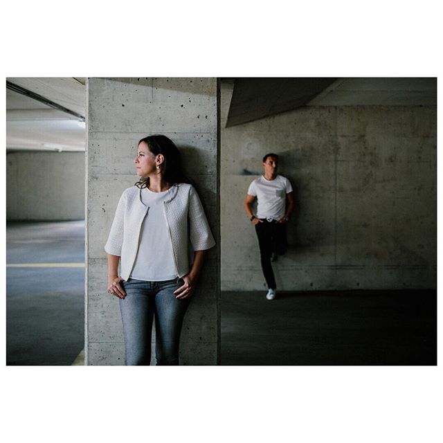 Two women lean against concrete walls in an urban parking garage, exuding calm and contemporary style.