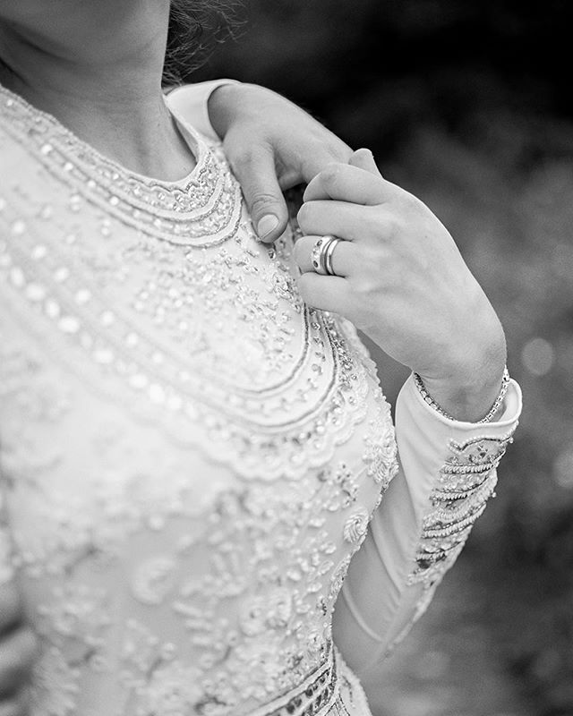 Close-up of a bride's hand with wedding rings on a dress, expressing love and commitment in a monochrome image.
