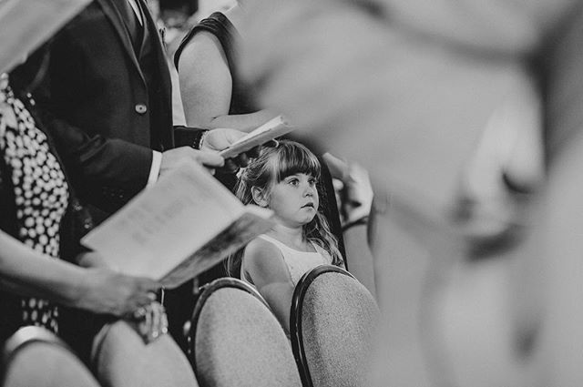 A young girl attends a wedding, sitting attentively amidst the guests in this black and white shot.