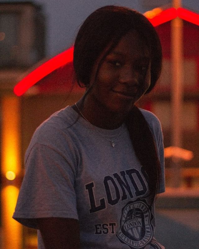 A smiling young woman poses outdoors in soft light wearing a graphic t-shirt.