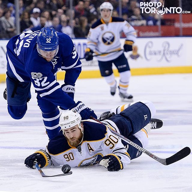 A dramatic ice hockey scene shows two players battling for the puck on the ice in a fast-paced game.